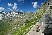 Woman hiking standing at Passo Barbacane and looking into valley, Sentiero Roma, Bergell range, Lombardy, Italy