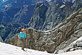 Frau steigt über Schneefeld auf, Felsen im Hintergrund, Sentiero Roma, Bergell, Lombardei, Italien