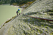 Woman climbing on a granite slab, lake in background, Raeterichsboden, Grimsel pass, Bernese Oberland, Switzerland