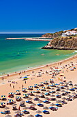 Holidaymakers sunbathing under beach umbrellas on the sandy beach at Praia do Tunel, Albufeira Beach, Algarve, Portugal, Europe