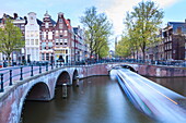 Long exposure of a tourist boat crossing canals Keizersgracht from Leidsegracht at dusk, Amsterdam, Netherlands, Europe