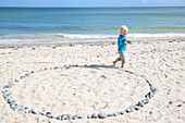 Boy walking along a circle of stones at beach, Rytsebaek, Mon island, Denmark