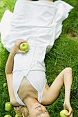 Young woman lying in grass, holding apples