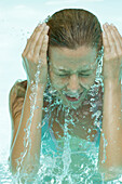 Young woman in pool, splashing face with water