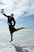Businesswoman barefoot on beach, jumping into the air with file in hand
