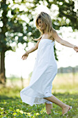 Young woman in dress walking in field, arms out