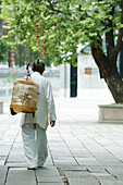 Elderly man wearing traditional Chinese clothing carrying bird cage over shoulder, rear view
