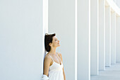 Woman leaning against column, eyes closed, smiling, hair tousled by breeze