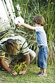 Little boy pouring water on his father's head as he works in garden