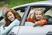 Mother and young daughter leaning out of car windows, waving