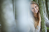 Young woman leaning against tree trunk, focus on background