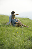 Couple sitting on meadow, man pointing toward distance