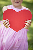 Girl holding paper heart, cropped