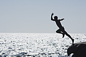 Teenage boy jumping into ocean, silhouette