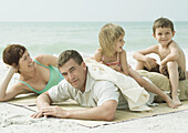 Family at the beach, parents lying on mat while children sit on father's back