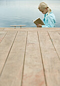 Girl reading book by water