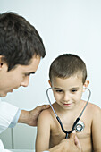 Doctor letting boy listen to own chest with stethoscope