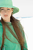 Young woman with long hair wearing sun hat on beach, waist up