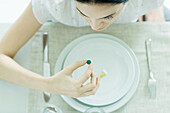 Woman sitting at empty plate holding vitamin