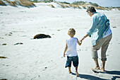 Child and adult walking on sand