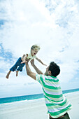 Man lifting child into air on beach
