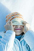 Girl lying on snow, pulling hat over eyes