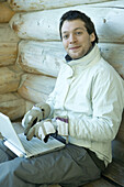 Man using laptop with gloves on, smiling at camera