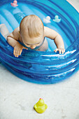 Baby in inflatable baby pool looking at rubber dusk on ground