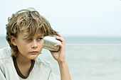 Boy holding tin can phone up to ear, looking away, portrait