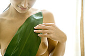 Nude woman holding leaf against breasts, cropped view