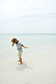 Boy on beach throwing rock toward ocean, full length