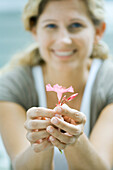Woman holding flower in hands, smiling at camera, focus on foreground