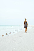 Woman in sundress walking at the beach, rear view