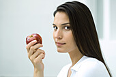 Woman holding apple, looking sideways at camera