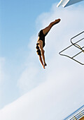 Woman in mid-dive, low angle view, full length, blue sky in background