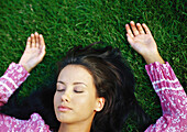Frau im Gras liegend mit geschlossenen Augen, Nahaufnahme