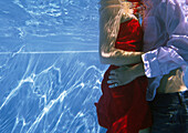 Fully clothed couple embracing in pool, underwater view