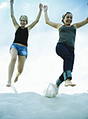 Women jumping on sand, low angle view
