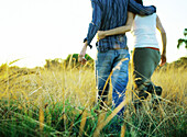 Couple walking through field, rear view, low section