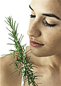 Woman's face with eyes closed smelling sprig of rosemary, close-up