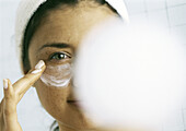 Frau trägt Feuchtigkeitscreme unter dem Auge auf, unscharfe Kompaktkamera im Bildvordergrund