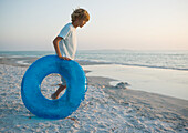 Boy rolling innertube on beach toward water