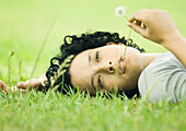 Junge Frau im Gras liegend mit Löwenzahnstängel im Mund