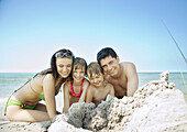 Family sitting on beach near pile of sand, portrait