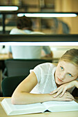 Female college student sitting at table in library, resting on book