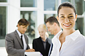 Young businesswoman smiling, associates talking about contract in background