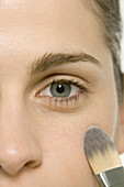 Frau trägt Make-up auf die Wange auf, Ausschnitt aus dem Gesicht