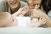 Parents smiling down at baby, mother holding baby's feet, cropped view