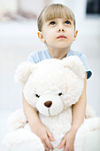 Little girl holding teddy bear, looking up
