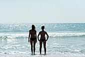 Teen girls standing side by side at the beach, looking at horizon